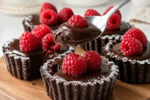 Raspberry chocolate ganache tartlets garnished beautifully on a plate