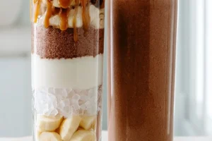 Creamy chocolate banana cheesecake smoothie served in a glass with banana slices.